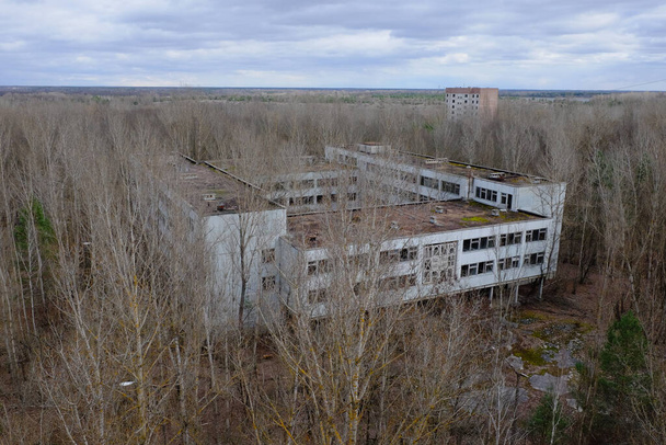 Заброшенное бетонное здание среди деревьев в Припяти. Вид с воздуха. Облачно, ландшафт. - Фото, изображение