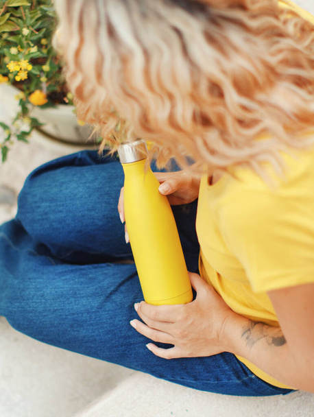Mujer joven en camiseta amarilla sosteniendo botella reutilizable amarilla  - Foto, imagen