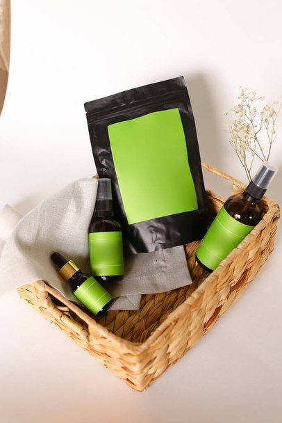Paquete doy negro y botellas de spray con productos cosméticos en canasta de mimbre, espacio verde para tu marca. - Foto, Imagen