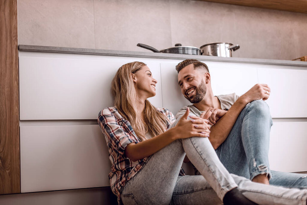 happy couple discussing something sitting on the kitchen floor - Фото, зображення