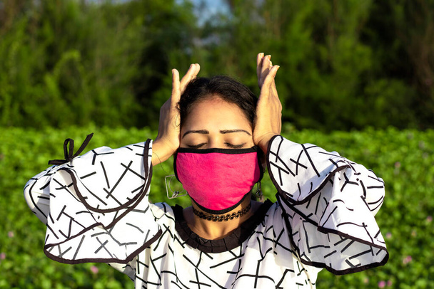 保護ピンクのフェイスマスクを着用し、自然な緑の背景にポーズスタイリッシュな女性。緊張感の強い若い女性のストレス排出頭痛. - 写真・画像