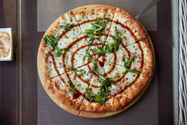 Pizza with arugula on a wooden plate on grey background in summer terrace. - Photo, Image