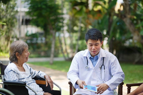 アジア人医師が高齢女性患者と車椅子で話す - 写真・画像