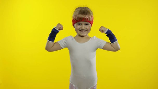 Sportliches Mädchen in weißer Sportbekleidung, das auf gelbem Hintergrund vereinzelt Muskeln zeigt. Workout für Kinder - Foto, Bild