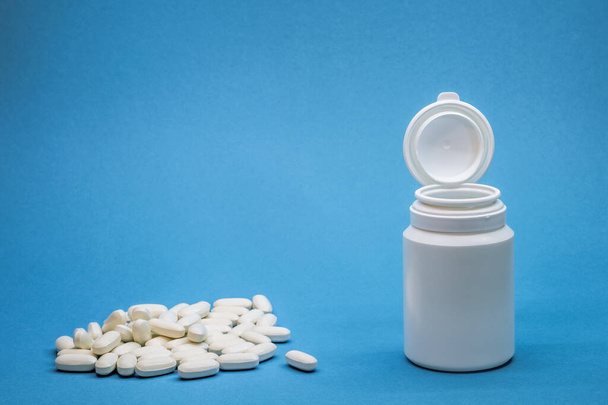 White bottle with a pile of oval tablets on a blue background. Background - Foto, Bild