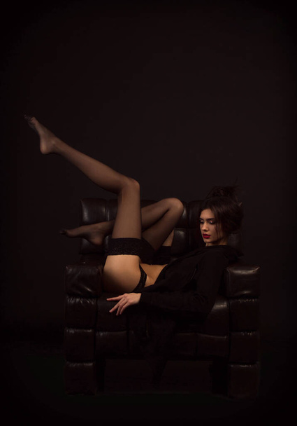 hermosa chica sentada en una silla de cuero con las piernas arriba. medias negras. - Foto, imagen