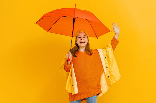Happy emotional child laughing and jumping. Kid with orange umbrella on colored red background. - Photo, image