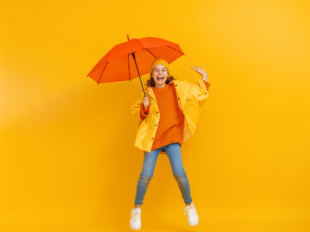 Happy emotional child laughing and jumping. Kid with orange umbrella on colored red background. - Foto, afbeelding