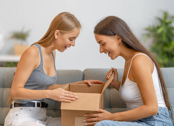 Beautiful young women are holding cardboard box sitting on sofa at home. - Foto, Bild