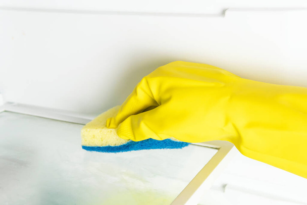 Ręka kobiety w żółtej rękawiczce czyszczącej półkę na lodówkę. - Zdjęcie, obraz