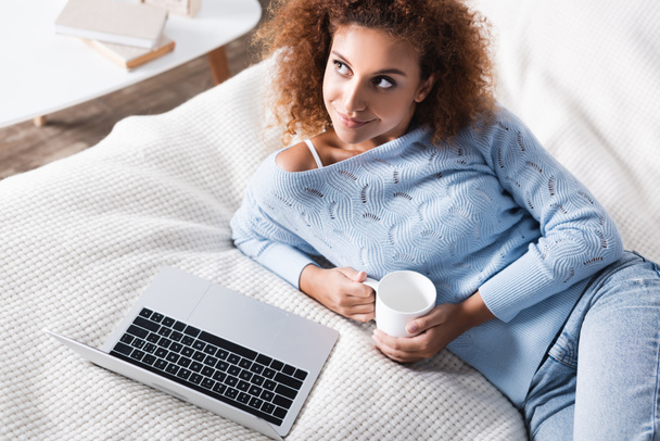 Korkea kulma näkymä nainen tilalla cup lähellä laptop sängyssä  - Valokuva, kuva