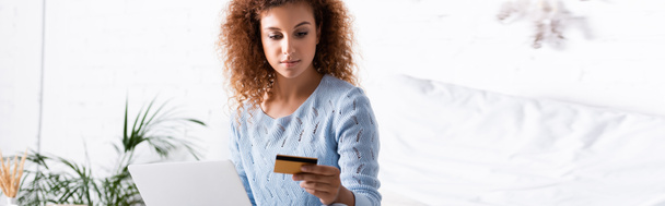 Cultivo panorámico de mujer pelirroja con tarjeta de crédito durante las compras en línea en casa  - Foto, imagen