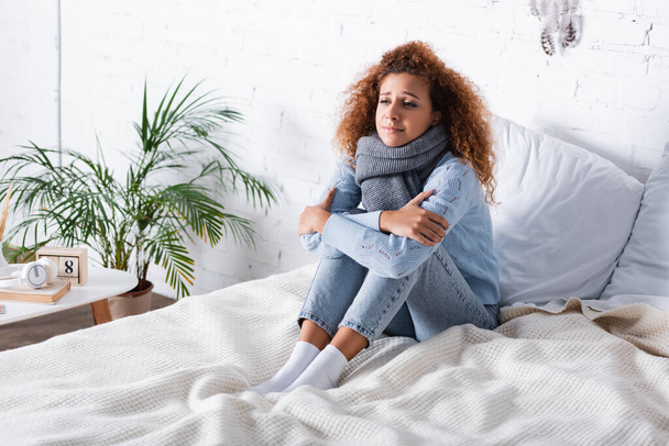 Νεαρή γυναίκα με μαντήλι που νιώθει κρύο στο κρεβάτι στο σπίτι  - Φωτογραφία, εικόνα