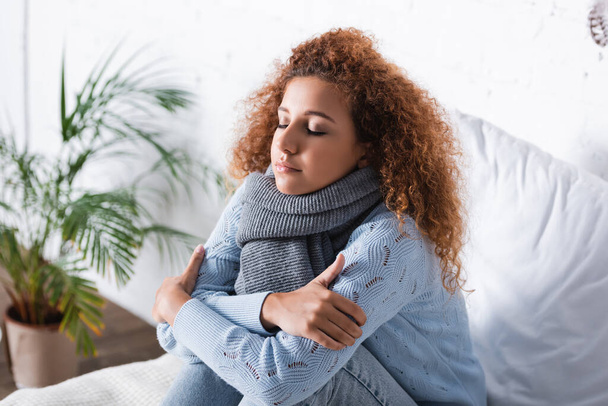 Red haired woman in scarf and sweater feeling cold on bed  - Photo, Image