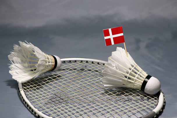 ミニデンマークの旗は、バドミントンラケットのネットと灰色の床の上にシャトルトックに置きます.  - 写真・画像
