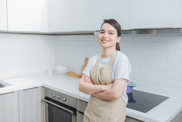 smiling, beautiful woman standing with crossed arms and looking at camera in kitchen - Fotografie, Obrázek