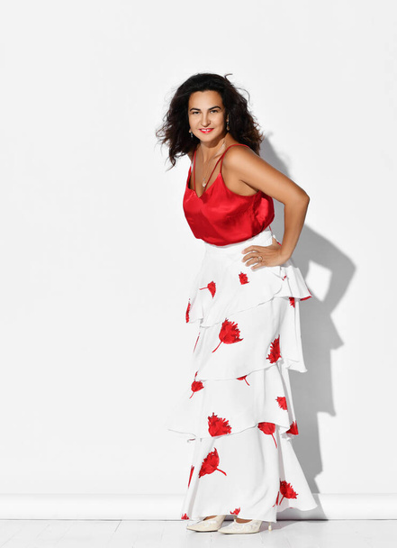Gorgeous woman hispanic dancer wearing red white gown with flower print dances Carmen flamenco holding hands on hips - Fotó, kép