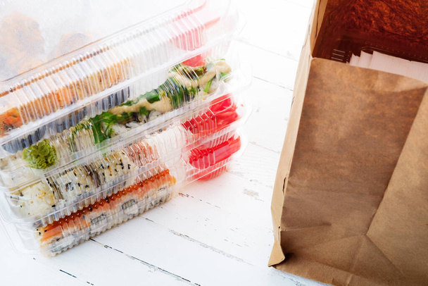 Пачка пластиковых коробок с наборами суши и бумажным пакетом. Доставка продуктов питания - Фото, изображение