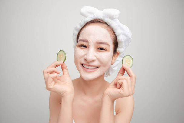 Young woman with clay facial mask holding cucumber slices isolated on white background - Foto, Imagen