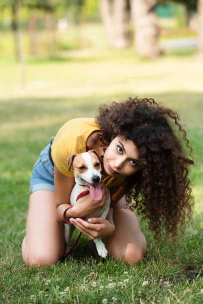Выборочный фокус молодой женщины, сидящей на траве и обнимающей собаку - Фото, изображение