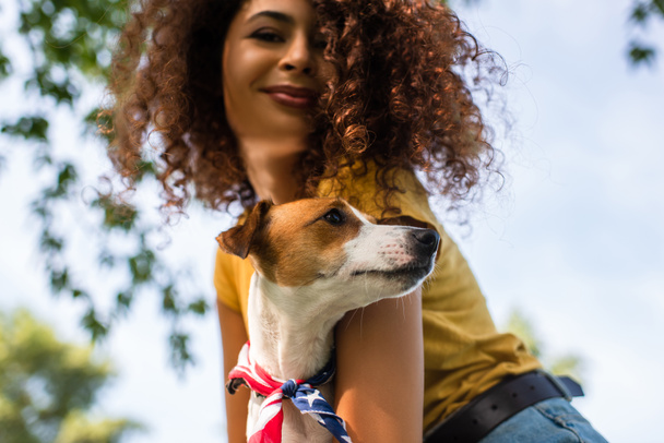 low angle view of joyful, curly woman holding jack russell terrier dog - Foto, Imagen