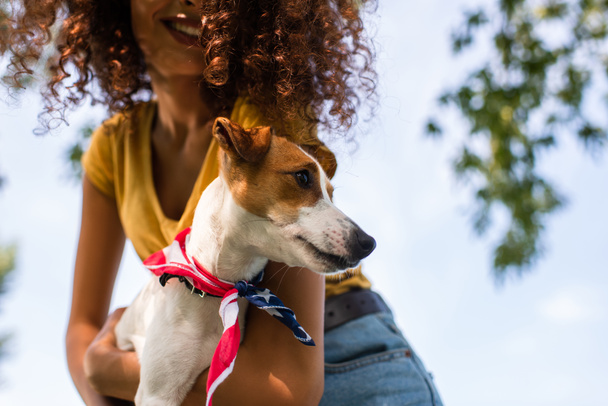 cropped view of curly woman holding jack russell terrier dog against blue sky - Фото, изображение