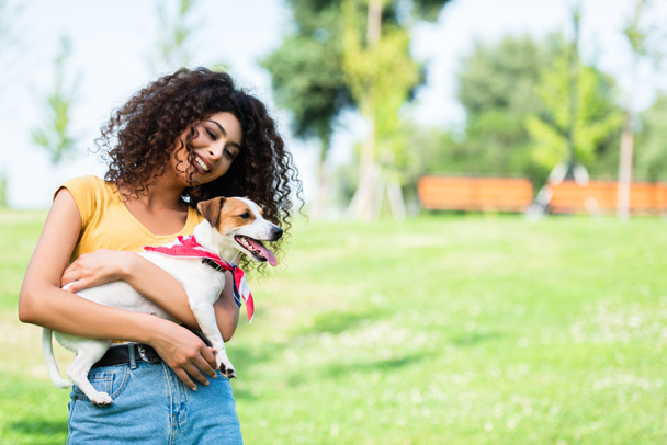 ενθουσιασμένοι γυναίκα σε καλοκαιρινή στολή αγκαλιάζει Jack Russell Terrier σκυλί στο πάρκο - Φωτογραφία, εικόνα