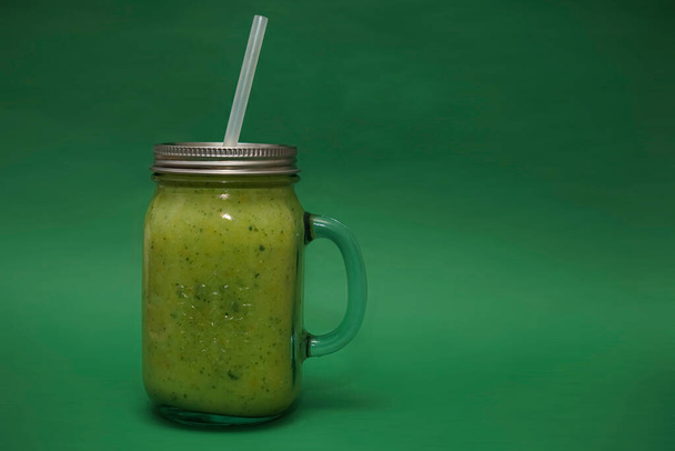 pot plein en verre, tasse avec un couvercle, poignée et paille isolé sur fond vert. smoothie  - Photo, image
