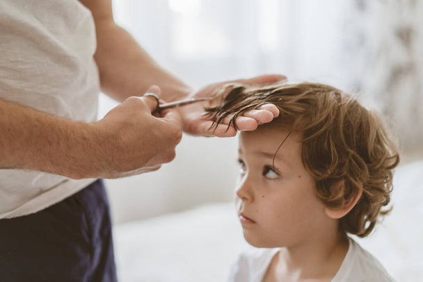 Baba odada oğlunun saçını kesiyor. Karantina sırasındaki aile, makas ve erkek ellerinde tarak. - Fotoğraf, Görsel
