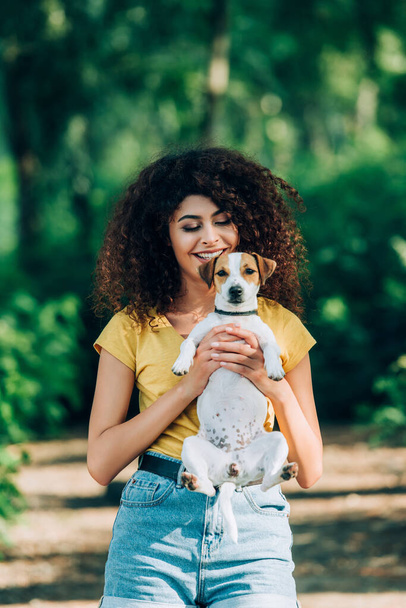 joyful woman in summer outfit holding jack russell terrier dog in park - Fotoğraf, Görsel