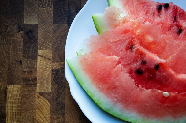 Close-up slices of watermelon on a white plate on a wooden table  with copy space. Ripe red watermelon cut into slices on a wooden background. Top view. - Φωτογραφία, εικόνα