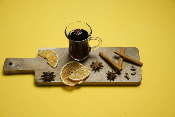 Um copo de vinho quente numa tábua de madeira com paus de canela e laranja seca. Vista superior - Foto, Imagem