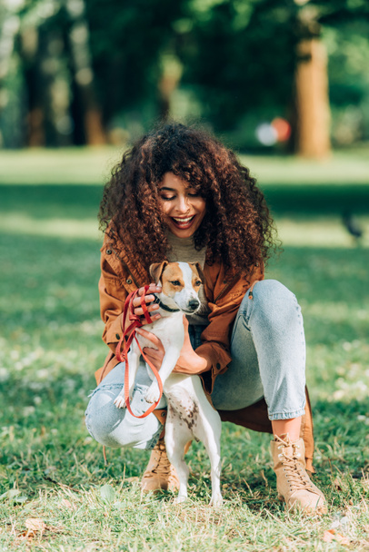 Selective focus of woman in raincoat petting jack russell terrier in park  - Photo, Image