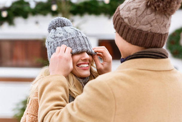 Romantyczna para bawiąca się na świeżym powietrzu w zimie, mężczyzna bawiący się kapeluszem dziewczyny - Zdjęcie, obraz