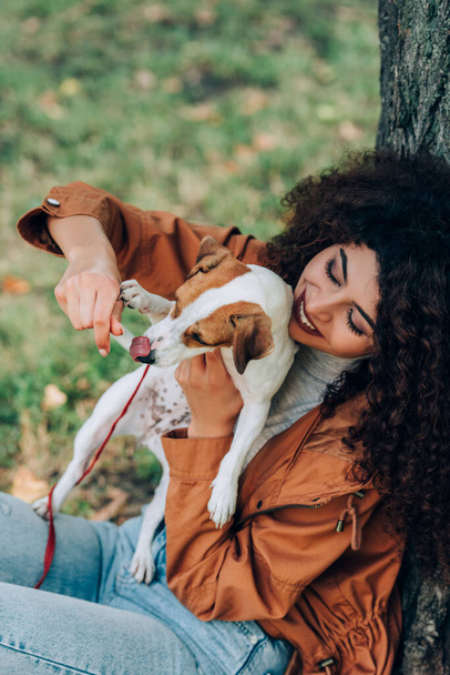 Selective focus of woman in autumn outfit playing with jack russell terrier in park - Photo, Image