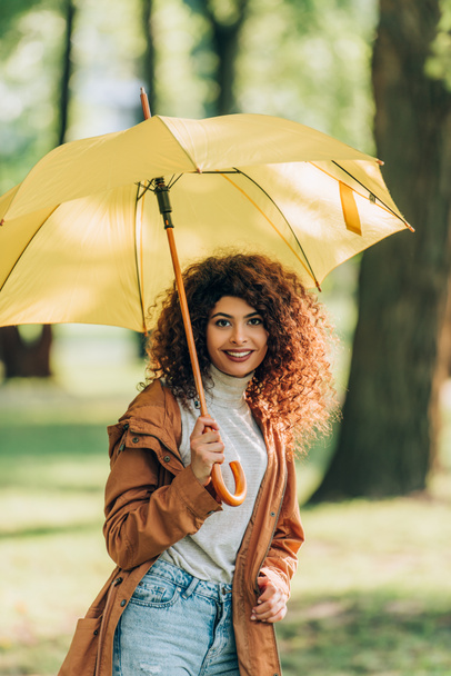 Giovane donna in abito autunnale che tiene l'ombrello e guarda la fotocamera nel parco  - Foto, immagini