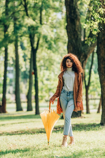 Selective focus of curly woman holding umbrella while strolling in park  - Foto, Imagem