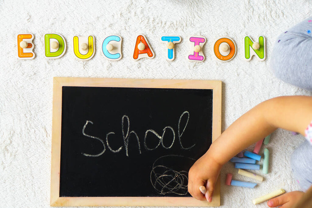 School board. The child draws on the board with chalk. Preparing for school. Education for the youngest. Preschool education in kindergartens. The word education is written in colored wooden letters - Fotoğraf, Görsel