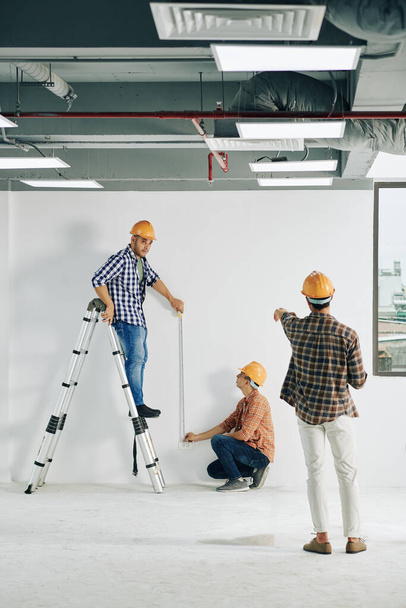 Entrepreneur s'est éloigné pour contrôler les travailleurs mesurant ligne droite sur le mur avec ruban à mesurer - Photo, image