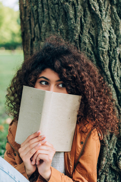 Selective focus of woman holding book near tree in park  - Zdjęcie, obraz
