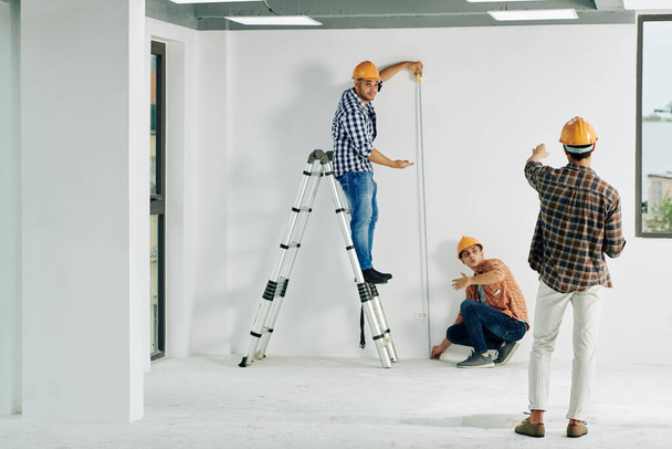 Equipo de trabajadores de la construcción en sombreros de pared de medición con cinta métrica - Foto, imagen