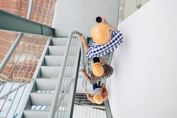 Travailleurs de la construction en casque de sécurité montant les escaliers les uns après les autres, vue du haut - Photo, image