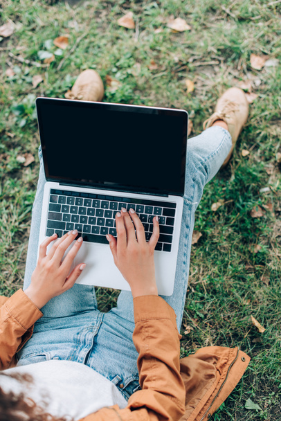 Top view of young woman in raincoat and jeans using laptop with blank screen in park  - Fotografie, Obrázek