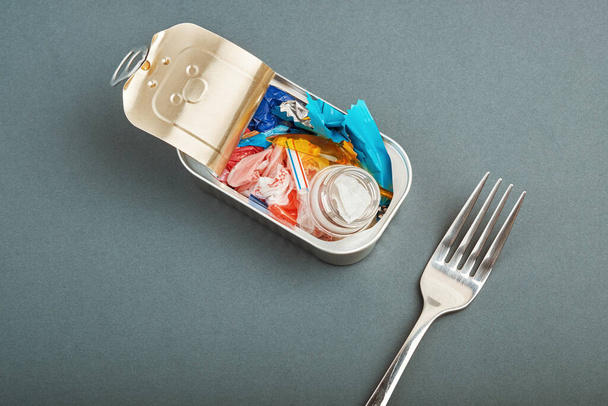 Lata abierta y tenedor. Residuos de plástico en lugar de pescado adentro. concepto de contaminación plástica oceánica - Foto, Imagen
