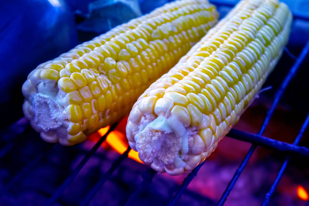 Maïs doré mûr sur le gril avec de la fumée et de la flamme sur fond de cendres. Barbecue végétarien sur le feu à l'extérieur. - Photo, image