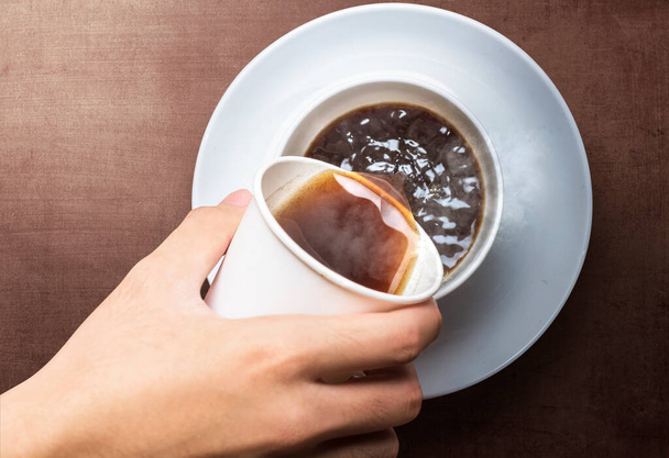 Рука наливає каву з чашки стиропіни на чашку чашки з чашкою чашки на столі. Міжнародний день кави - Фото, зображення
