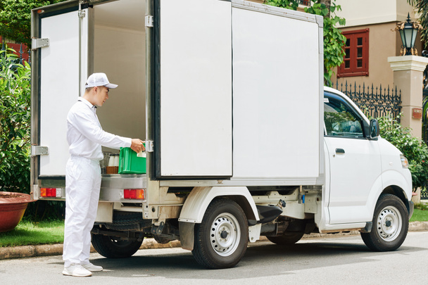 Чоловік в білій формі бере пластикову ящик зі скляними пляшками молока з фургона
 - Фото, зображення