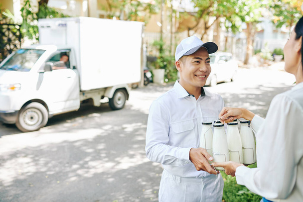 Milkman sonriente entregando botellas de leche a un cliente bastante femenino - Foto, imagen