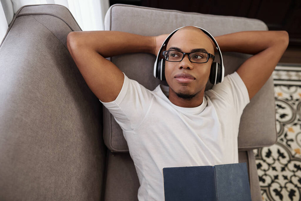 Muotokuva hymyilevä unenomainen nuori Musta mies lepää sohvalla kuulokkeissa ja katselee pois - Valokuva, kuva