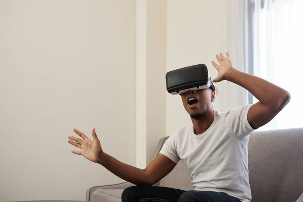 Ενθουσιασμένος νεαρός άνδρας παίζει τρομακτικό παιχνίδι σε γυαλιά εικονικής πραγματικότητας - Φωτογραφία, εικόνα
